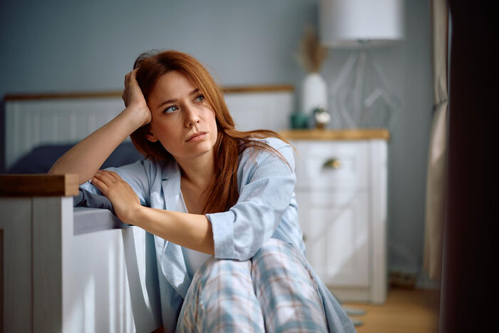 A woman sits on the floor by her bed, looking sad and contemplative about reasons people became affair partners.
