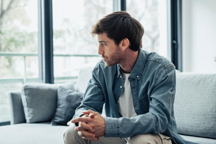 A pensive man sitting on a couch, reflecting on decisions as affair partners.