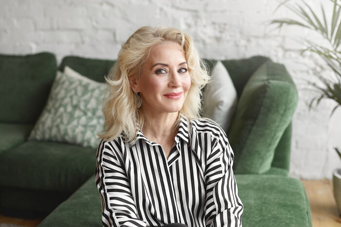 A mature woman with blonde hair and a striped shirt smiles confidently, representing the diverse reasons of affair partners.