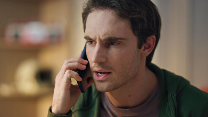 A man with a serious expression talks on a phone, possibly discussing issues related to affair partners.
