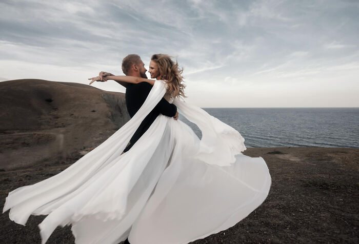 A couple dancing on a cliff overlooking the ocean. The woman's white dress flows in the wind, symbolizing affair partners.