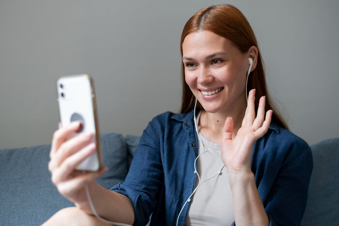 A smiling woman waves at her phone during a video call, discussing reasons people became affair partners.