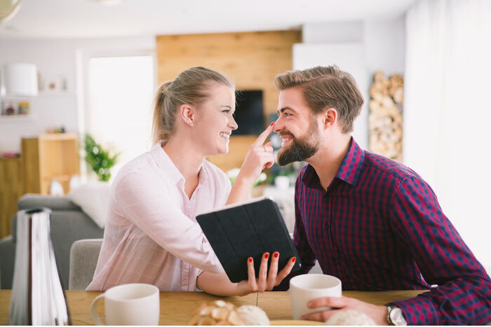 A happy couple at a table, with one playfully touching the other's nose, contrasting with affair partners.