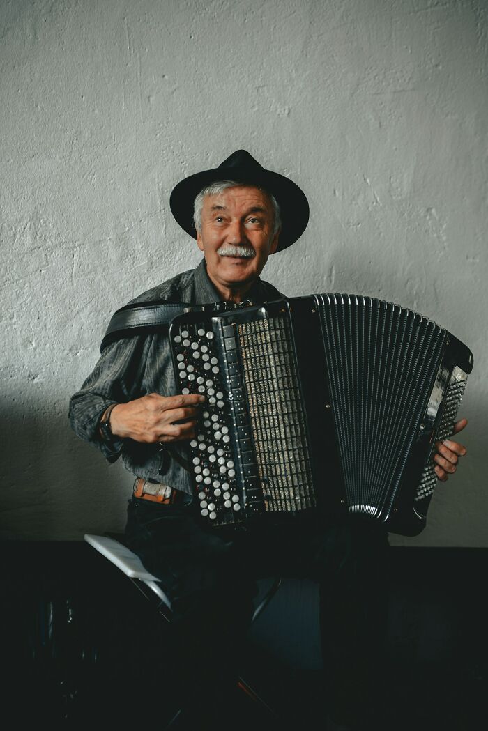 An older man with a mustache and hat happily playing an accordion. Showcases interesting neighbors.