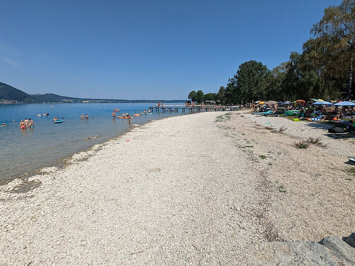 Europe suffers brutal drought: a crowded beach with people swimming, revealing low water levels and exposed gravel.