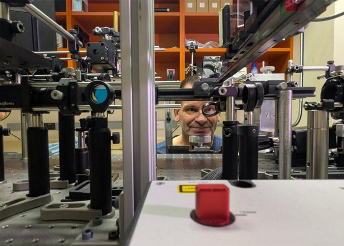 A scientist's face peering through complex optical lab equipment, highlighting the new color Olo research.
