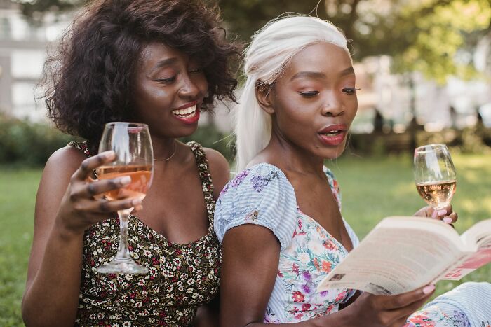 Two women enjoying wine and a book outdoors, sharing insider knowledge from different industries.