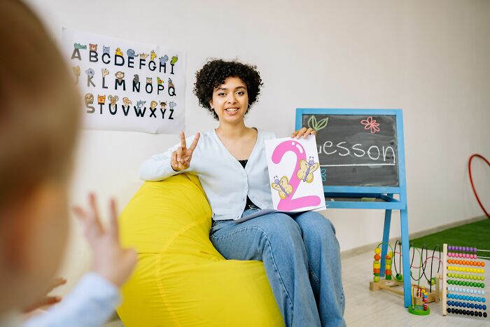 A teacher with curly hair and a child showing hand gestures for number two, sharing insider knowledge of education.