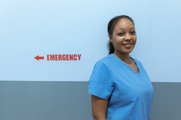 A smiling female healthcare worker in blue scrubs standing next to an emergency sign. Gain insider knowledge from different industries.