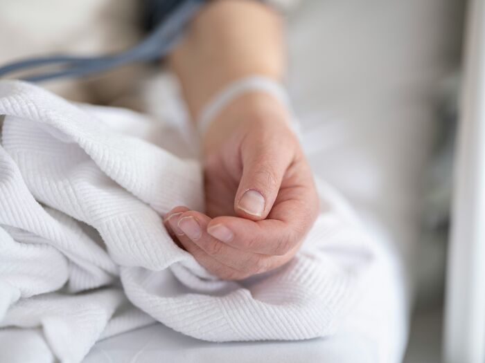 A person's hand with an IV on a white hospital bed, illustrating insider knowledge about the healthcare industry.