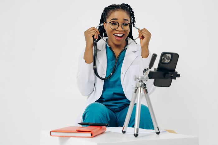 A happy female doctor in a white coat with a stethoscope records a video on a smartphone, sharing insider knowledge.