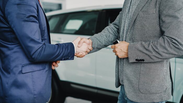 Two men shaking hands in front of a car, exchanging insider knowledge from different industries.
