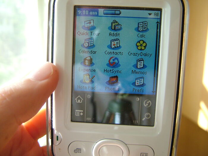 A hand holds an old handheld device with a grid of colorful app icons on the screen, representing companies that used to dominate the market.