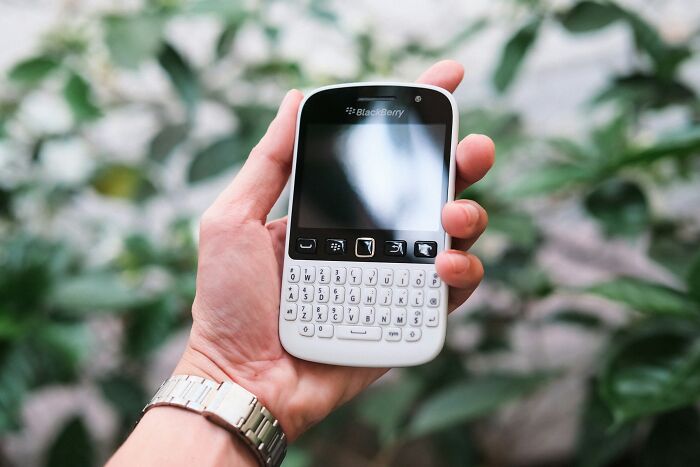 A hand holding a white Blackberry phone, a company that used to dominate the market.