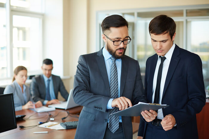 Two businessmen in suits review documents in an office, illustrating leadership decisions of companies that used to dominate the market.