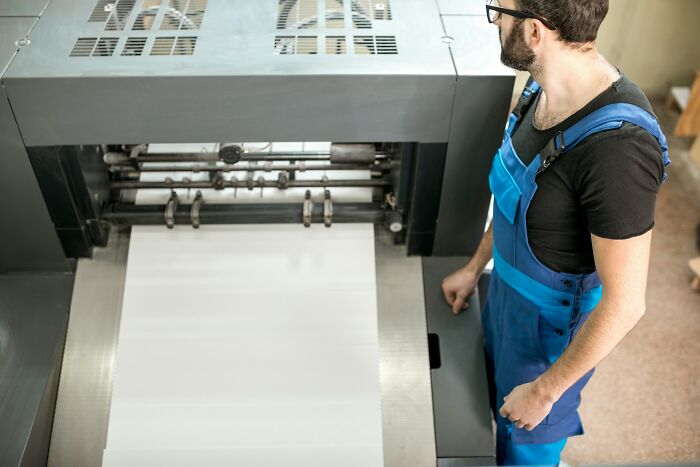 A man in overalls operates a large printing machine, symbolizing companies that used to dominate the market.