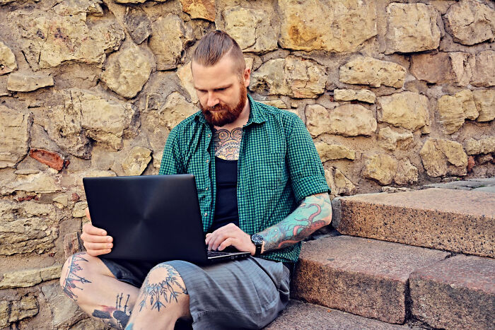 A man with tattoos working on a laptop, representing how poor decisions can lead companies to ruin.