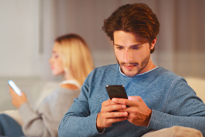 A man looking at his phone with a woman in the background, representing a guy and his girlfriend dealing with vitiligo.