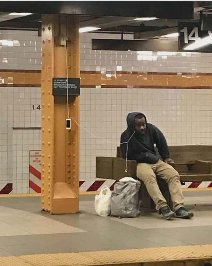 A man charges his phone at a subway station on a pillar, one of many pics people cannot explain.
