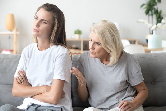 A young woman with crossed arms turning away from an older woman talking to her, showing difficult MILs.