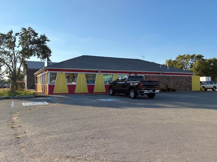 A red and yellow building, a building pretending to be something else, with yellow awnings and a black truck parked in front.
