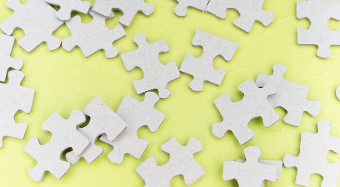 A pile of grey puzzle pieces scattered on a light green background, representing rebus puzzles and problem-solving. A pile of grey puzzle pieces scattered on a light green background, representing rebus puzzles and problem-solving.