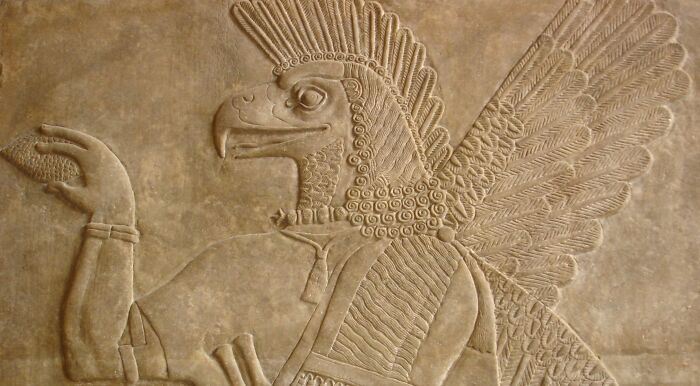 Ancient Assyrian relief of a winged genie, an important historical figure, holding a cone and bucket in a museum. Ancient Assyrian relief of a winged genie, an important historical figure, holding a cone and bucket in a museum.