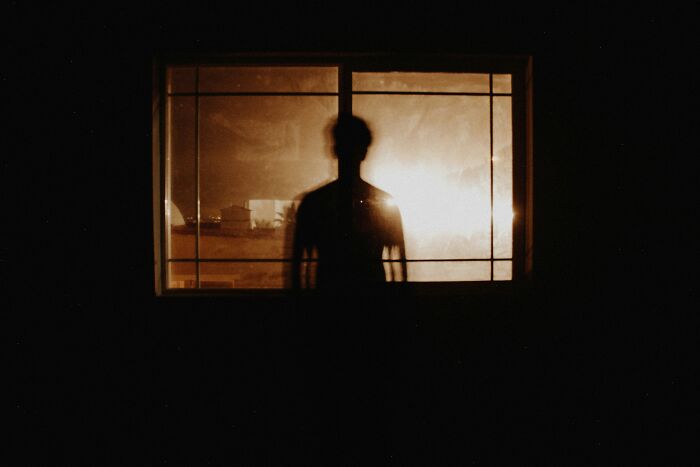 A silhouette of a person standing behind a window at night, symbolizing the fear teachers experience.