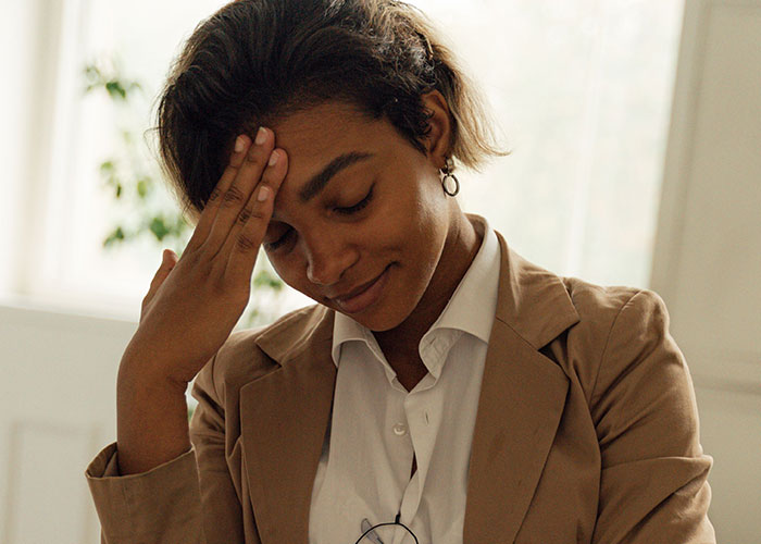 A woman with short hair, touching her forehead, looking stressed, depicting wild ways women caught their soulmates cheating.