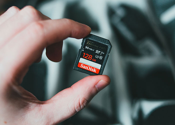 A hand holding a Sandisk SD card, used in wild ways women caught their soulmates cheating, with a 128 GB capacity.