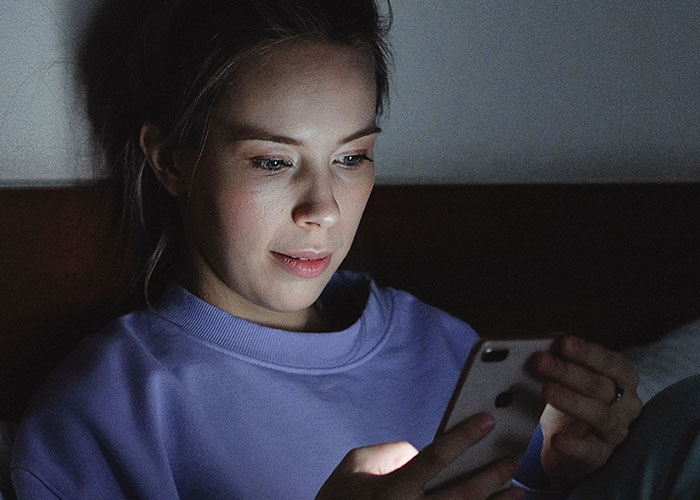 A woman looks at her phone in the dark, illustrating a woman catching her soulmate cheating.
