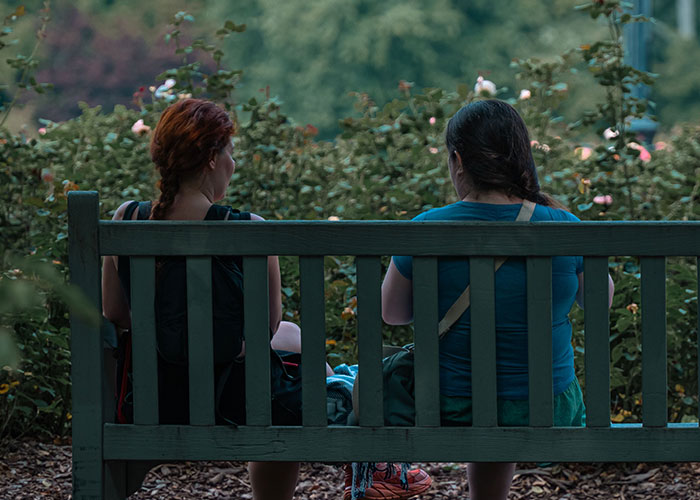 Two women sit on a bench in a garden, discussing ways women caught their soulmates cheating.