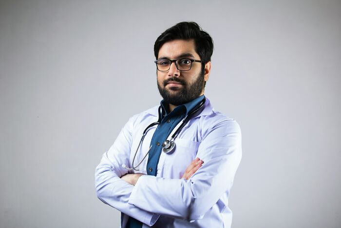 A male doctor with a beard and glasses stands with crossed arms, portraying a doctor involved in unhinged things doctors say.