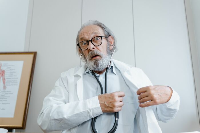 An elderly male doctor with a beard and glasses, looking surprised while using a stethoscope, highlighting things doctors said.