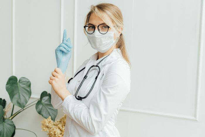 A female doctor in a white coat and glasses, wearing a mask and putting on blue gloves, highlighting things doctors said.