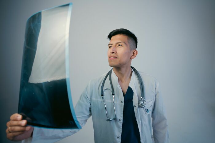 A male doctor in scrubs and a white coat holding up and examining an X-ray, highlighting things doctors said.