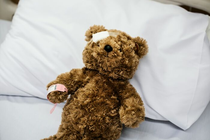 Injured teddy bear in a hospital bed with a bandage, representing unhinged doctor interactions.