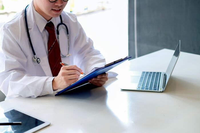 A doctor reviews a chart at a desk with a laptop, reflecting on unhinged things doctors say to patients.