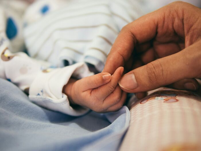 An adult's finger holds the tiny hand of a baby, symbolizing the vulnerable experience with doctors' unhinged comments.