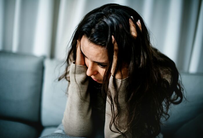 A woman sits on a couch, holding her head in her hands, looking distressed; illustrating unhinged things doctors said.