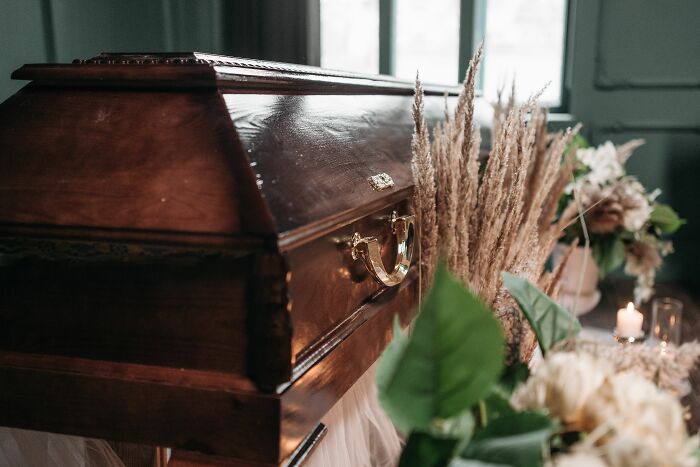 A dark wooden coffin with a golden handle, surrounded by dried flowers, evoking shivers from strange experiences.