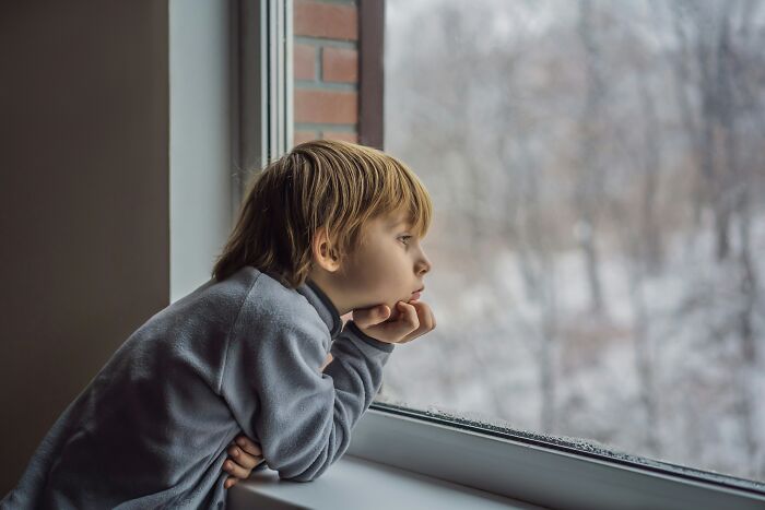 A young boy looks out a window on a cold, winter day, lost in thought, reflecting on strange experiences that still make people shiver.