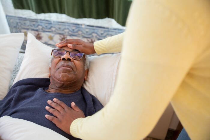 An older man lying in bed with someone checking his forehead, a strange experience that makes people shiver.