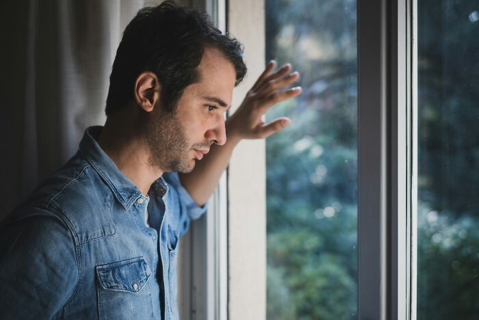 A man looking thoughtfully out of a window, recalling strange experiences that make people shiver.