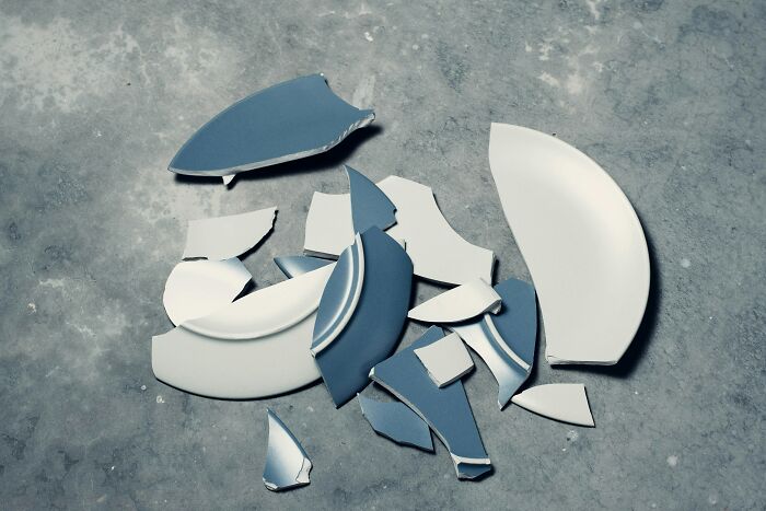 Broken pieces of blue and white ceramic plates scattered on a concrete surface, representing strange experiences that make people shiver.