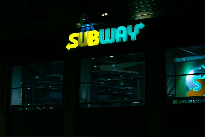 The glowing Subway sign at night, the yellow and blue letters visible, a place where strange experiences might occur.