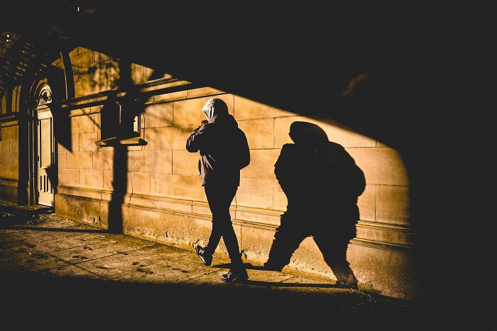 A person in a hoodie walking down a dark alley with a long shadow, a strange experience that makes people shiver.