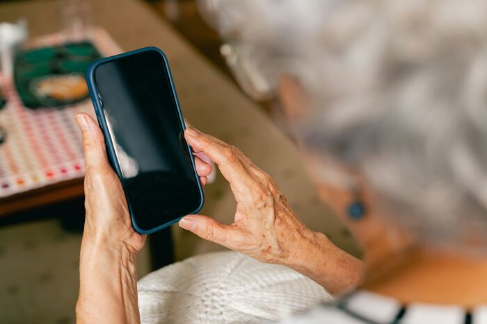 Elderly woman's hands holding a smartphone, a strange experience for some. The phone has a blank screen.