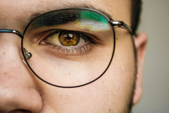 A close-up of a person's eye behind glasses, reflecting light, representing strange experiences.