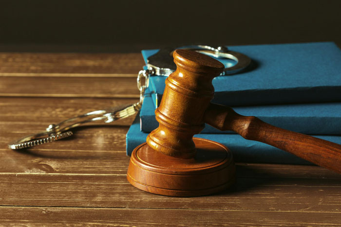A gavel and handcuffs on blue books, representing a criminal trial and legal proceedings.